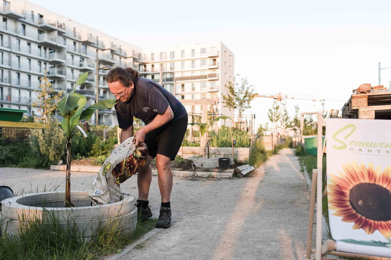 Ein Mann befüllt ein Pflanzgefäß mit Pflanzerde in einem Gemeinschaftsgarten.