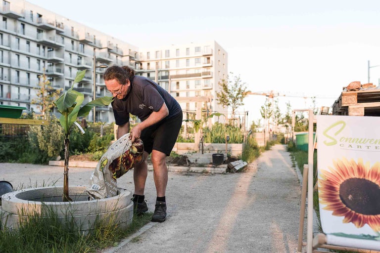 Ein Mann befüllt ein Pflanzgefäß mit Pflanzerde in einem Gemeinschaftsgarten.