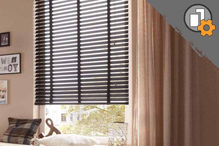 Zimmer mit schwarzen Jalousien und Vorhängen am Fenster.