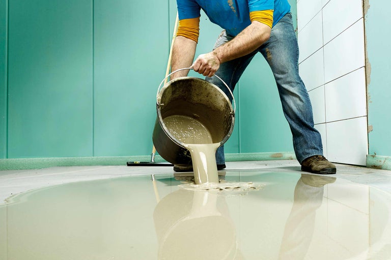 Handwerker gießt Ausgleichsmasse aus Eimer auf Boden