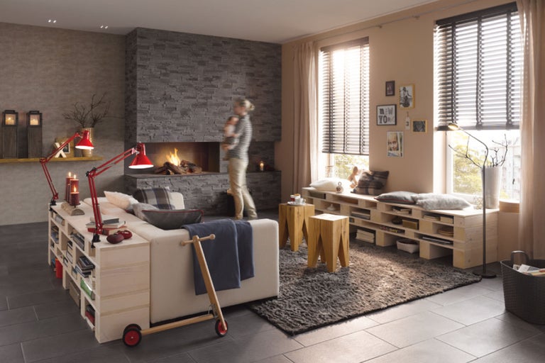 Wohnzimmer mit Kamin, Sofa mit Bücherregal, Holzschemel und Holzjalousien