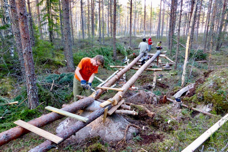 Männer bauen eine Holzbrücke in einem Wald.