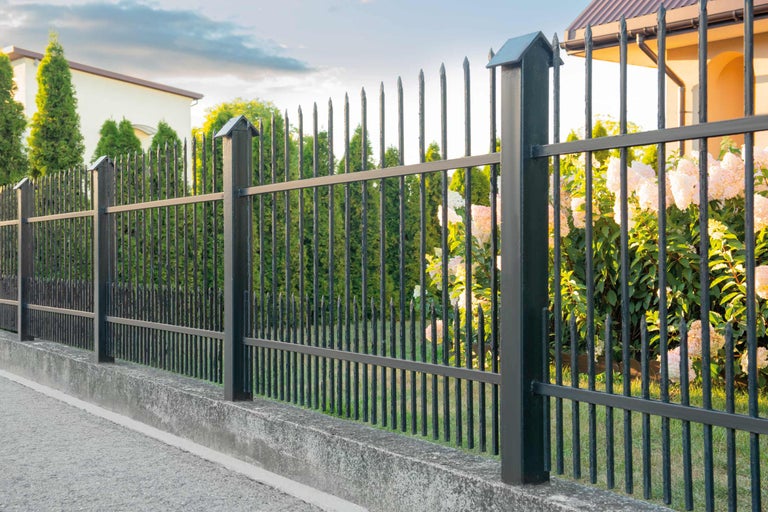 Schwarzer Metallzaun mit spitzen Stäben und Betonfundament um ein Grundstück.