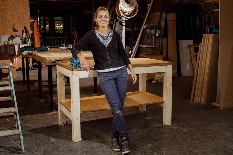 Frau lehnt an einer Werkbank aus Holz mit Schraubstock