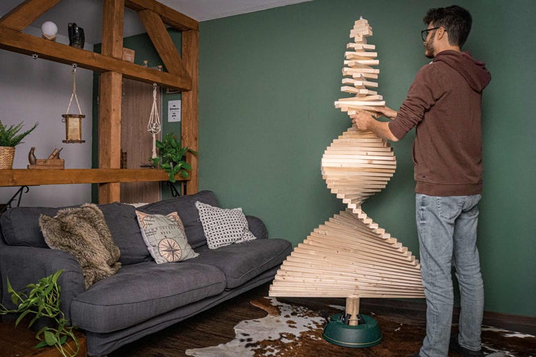 Mann baut einen hölzernen Design-Weihnachtsbaum im Wohnzimmer.