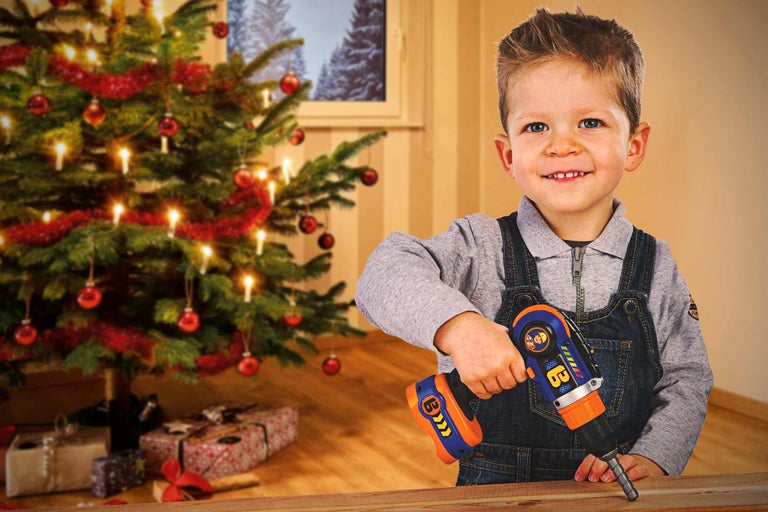 Junge mit Spielzeugbohrmaschine vor einem geschmückten Weihnachtsbaum