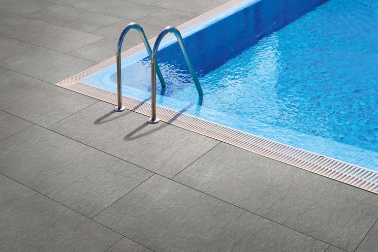 Graue Terrassenfliesen neben einem Swimmingpool mit Leiter.