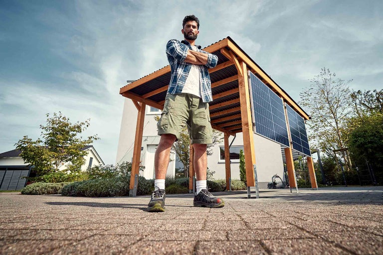 Mann mit gekreuzten Armen vor einem Carport mit Solaranlage
