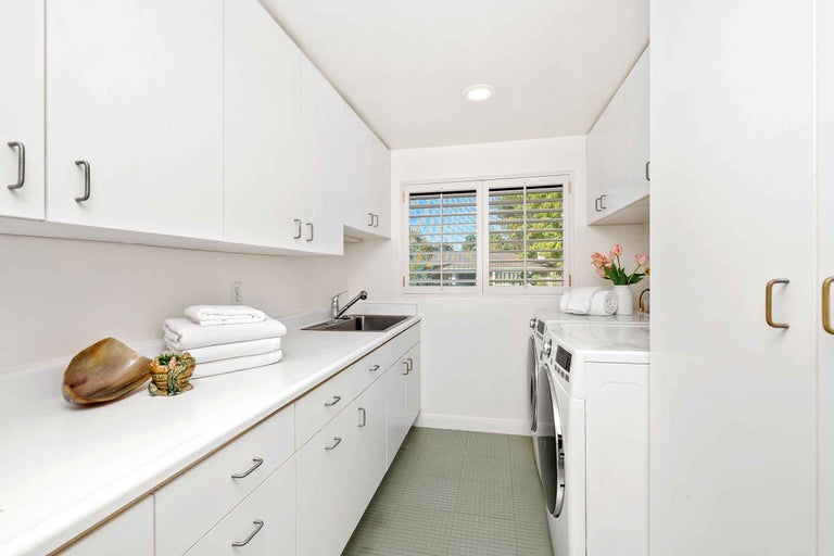 Heller Waschraum mit Waschmaschine, Trockner, Spüle und weißen Schränken