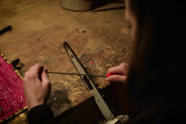 Eine Person schärft eine Kettensäge mit einem Schärfwerkzeug auf einer Werkbank.