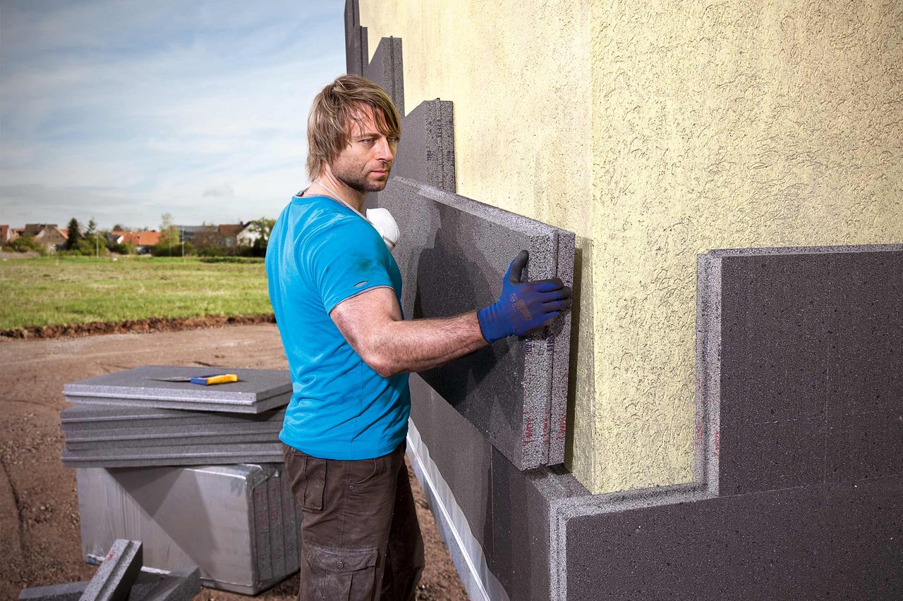 Mann montiert Fassadendämmplatten an einer Hauswand