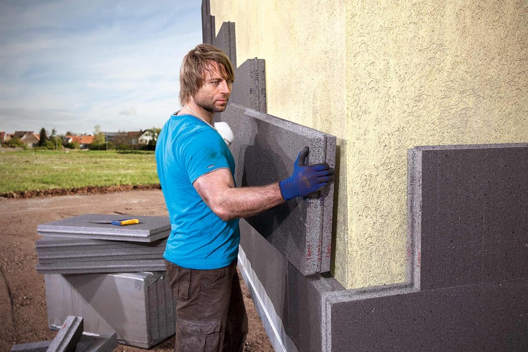 Mann montiert Fassadendämmplatten an einer Hauswand