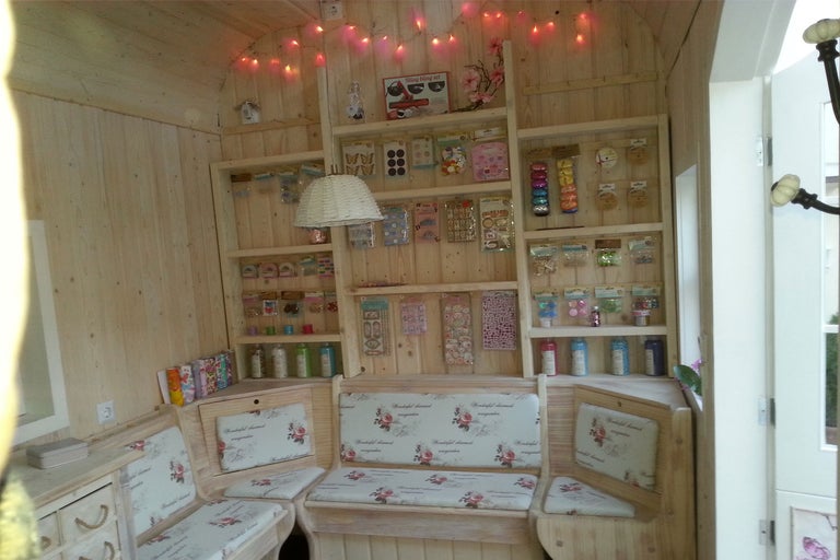 Helle Holzhütte mit Regalen, die Bastelmaterialien und eine Sitzecke mit floralen Kissen zeigen