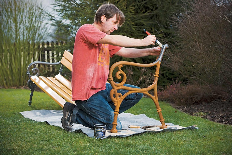 Mann streicht Gartenbank mit Metallschutzlack im Garten