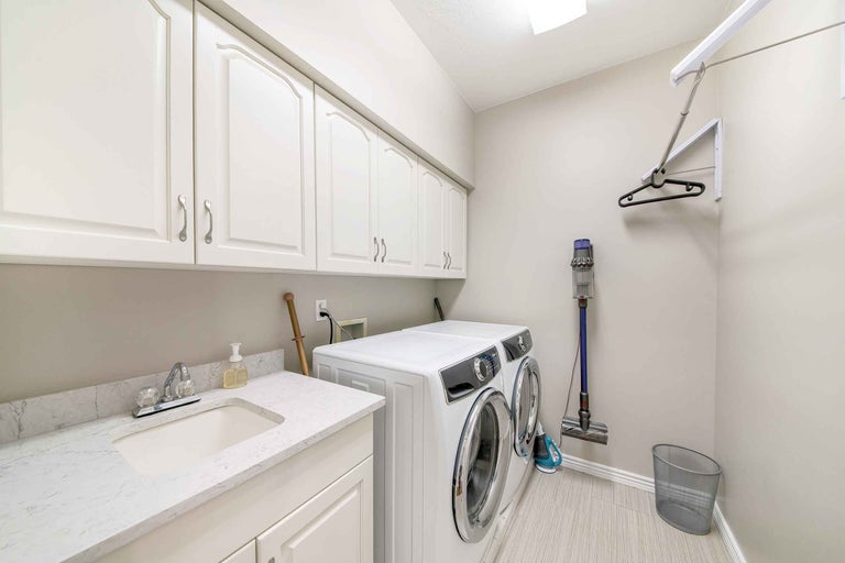 Waschküche mit Waschmaschine, Trockner, Spüle, Schränken und Staubsauger