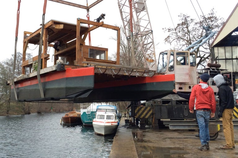 Ein Kran hebt ein Hausboot über das Wasser.