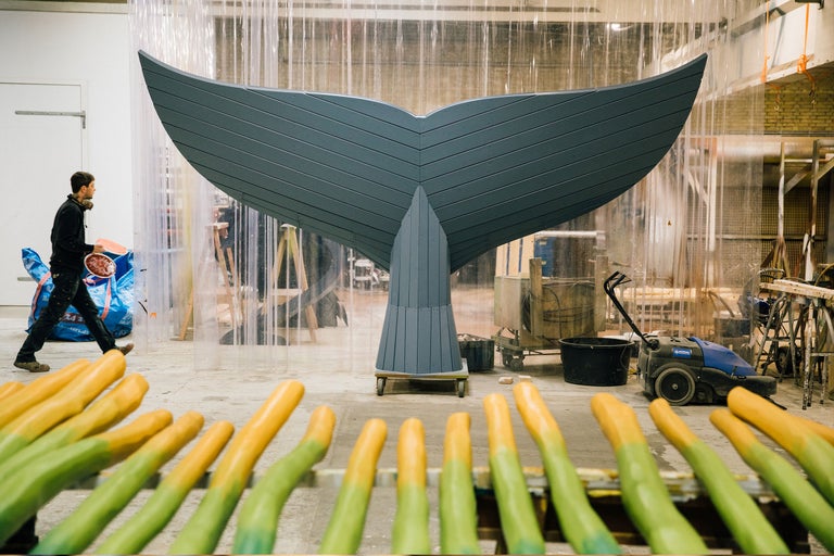 Werkstatt Szene mit einem großen hölzernen Walschwanz auf einem Rollbrettwagen und bemalten Holzpflöcken im Vordergrund