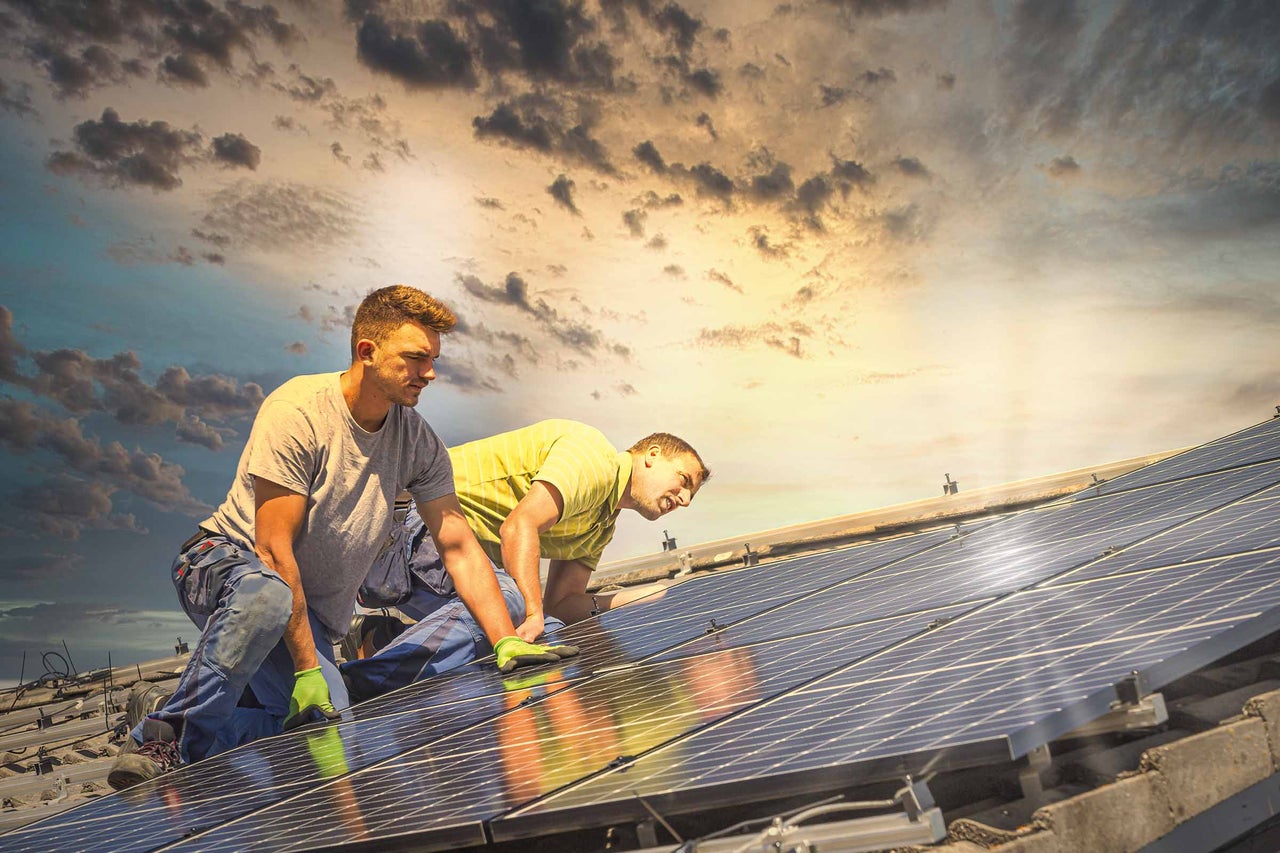 Zwei Installateure montieren Solarmodule auf einem Dach.