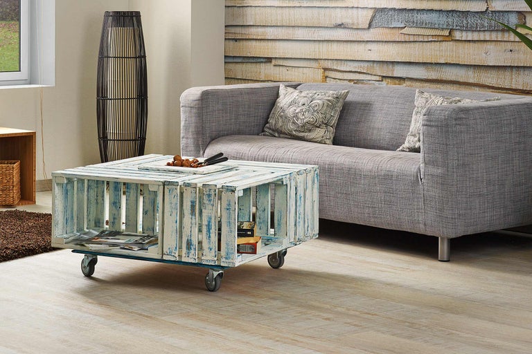 Wohnzimmer Szene mit grauem Sofa, Stehlampe und einem Couchtisch aus Holzkisten auf Rollen.