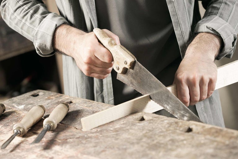 Mann sägt Holzbrett mit Handsäge auf Werkbank, Stecheisen liegen bereit