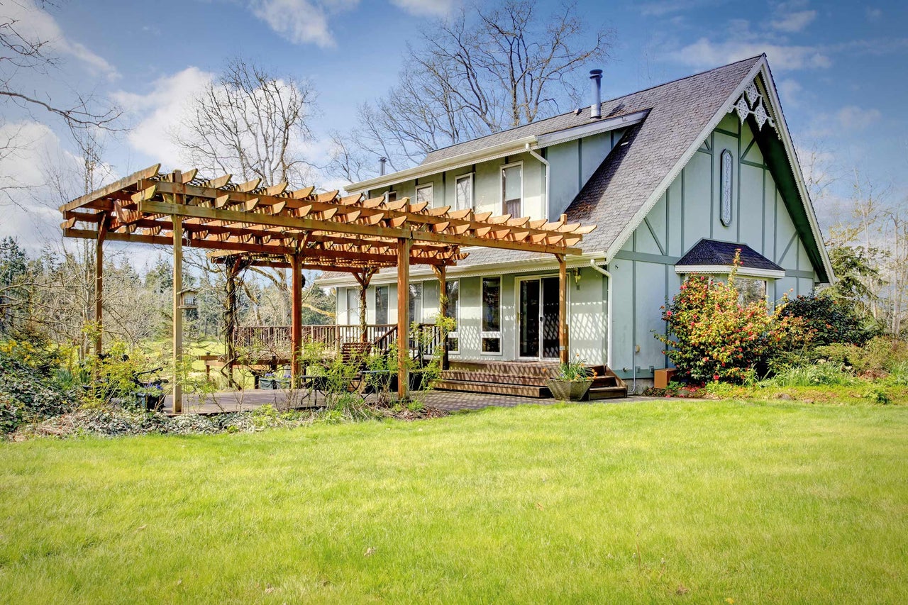 Ein Haus mit einer Holzpergola, einer Terrasse und einem Rasen.