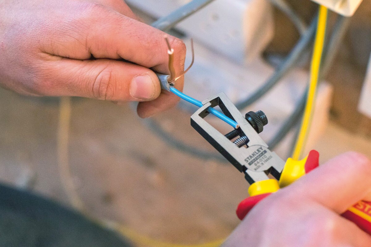 Elektriker mit Abisolierzange zum Abisolieren eines Kabels.