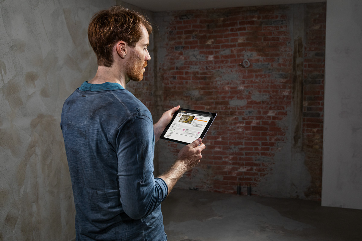 Mann mit Tablet-Computer in einem Rohbauzimmer mit Ziegelwand.