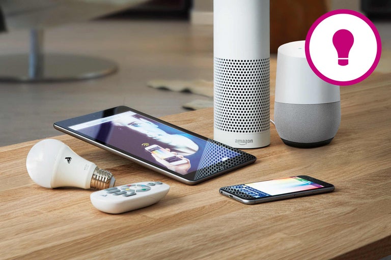 Smart Home System mit Lautsprechern, Tablet, Smartphone, Glühbirne und Fernbedienung auf einem Holztisch