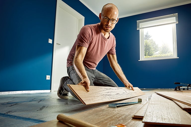 Ein Mann verlegt Laminatboden in einem Raum mit blau gestrichenen Wänden.