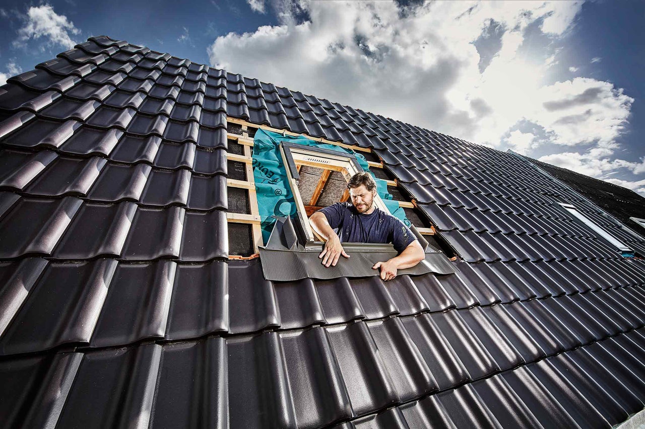 Handwerker montiert Dachfenster auf einem Dach mit Dachziegeln