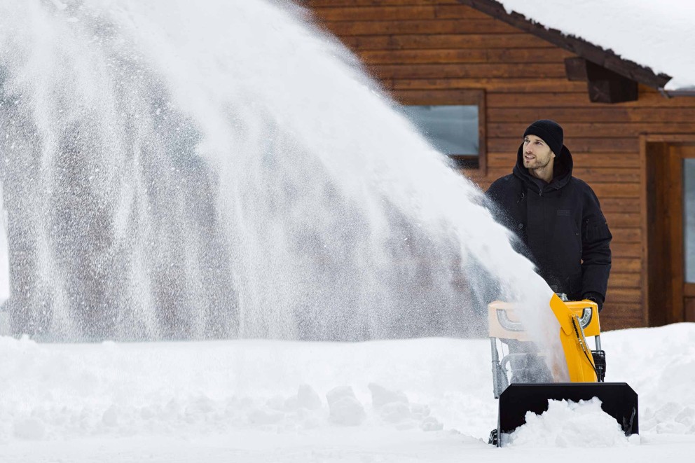 Mann benutzt eine Schneefräse vor einem Haus.