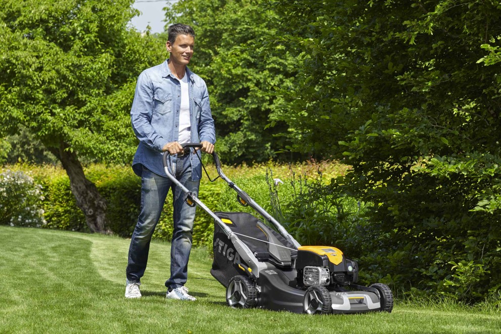 Mann mäht Rasen mit einem Rasenmäher im Garten.
