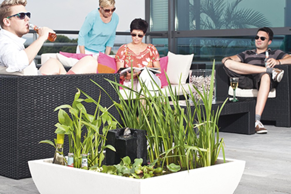 Szene mit Gartenmöbeln, Wasserpflanzen und entspannten Personen auf einer Terrasse