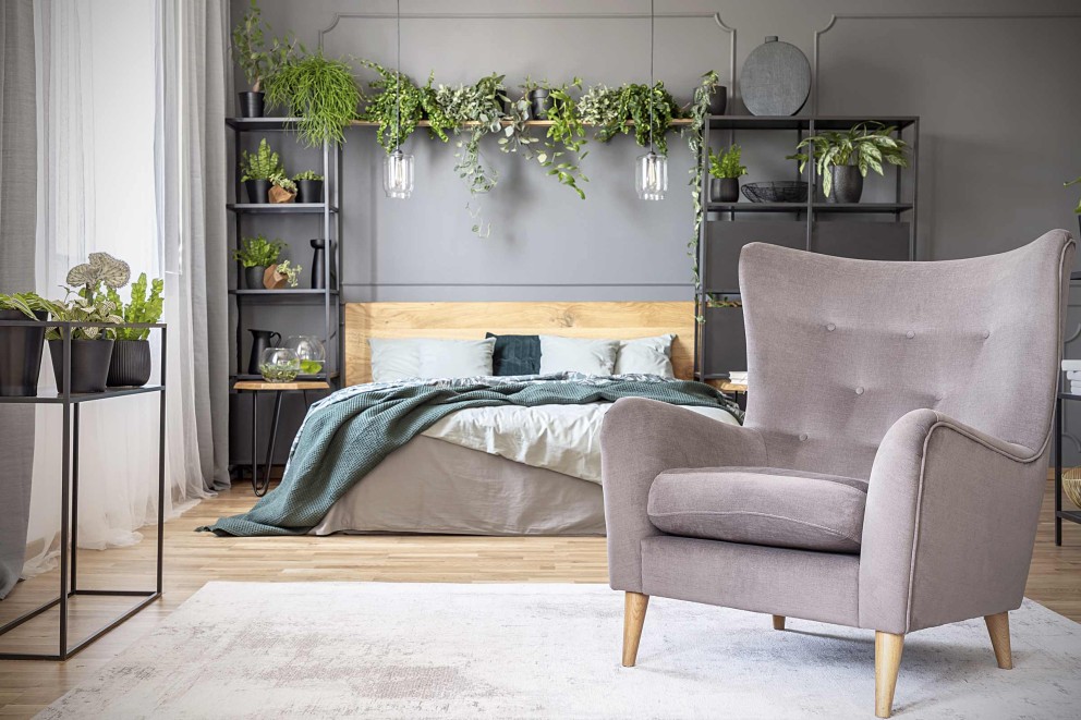 Schlafzimmer mit Bett, Sessel, Regalen und Zimmerpflanzen