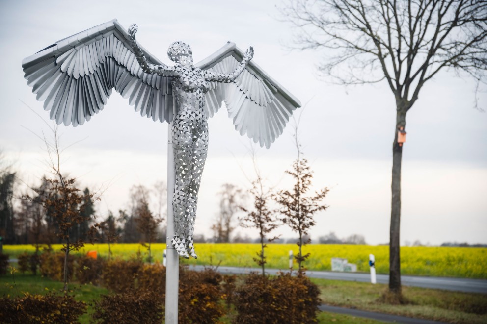 Engelsfigur aus Edelstahl an einer Stange, die in der Landschaft steht.