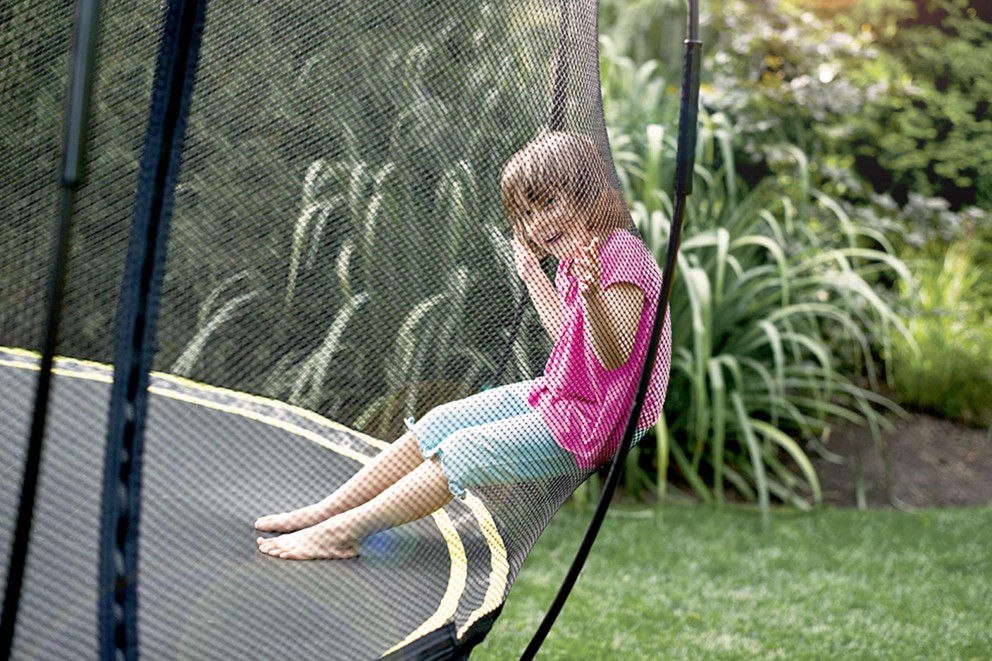 Mädchen sitzt im Gartentrampolin mit Sicherheitsnetz