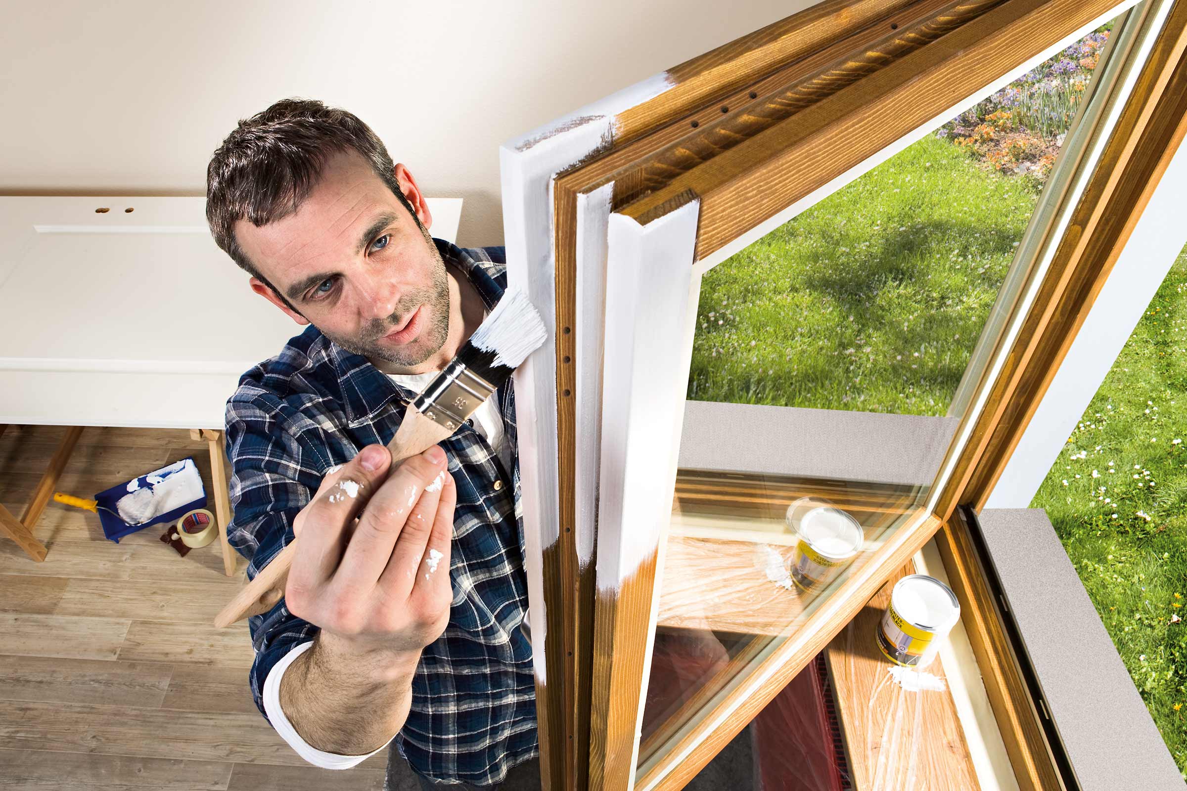 Mann streicht mit einem Pinsel einen Holzfensterrahmen mit Lack.