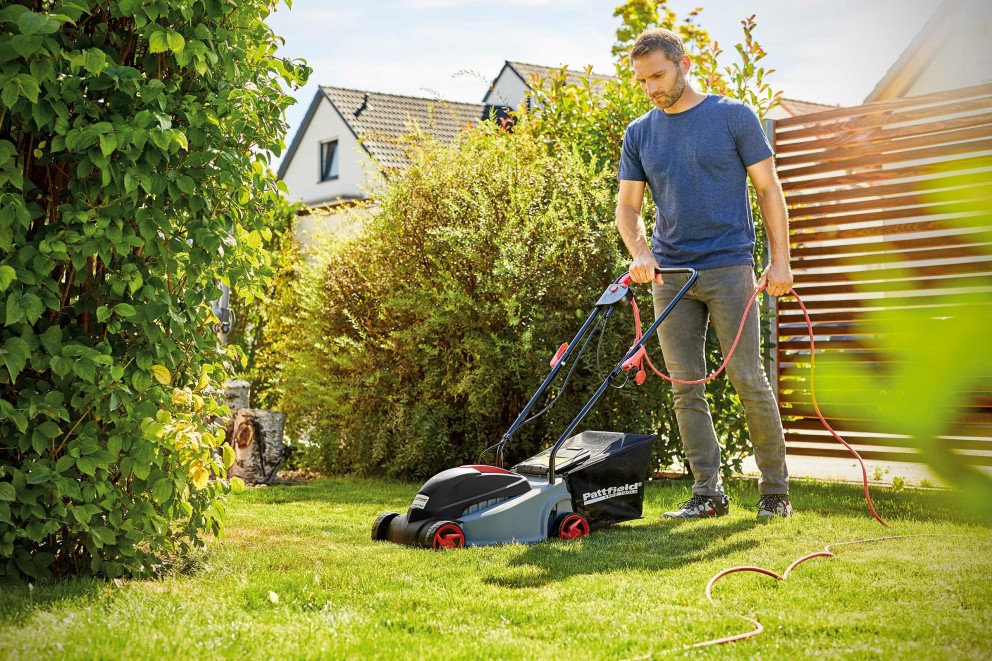 Mann mäht Rasen mit einem elektrischen Rasenmäher im Garten.