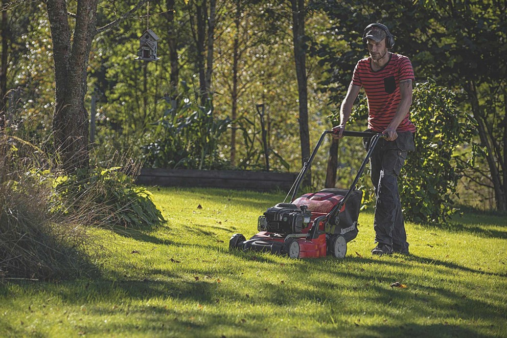 Mann mäht Rasen mit einem Rasenmäher im Garten.