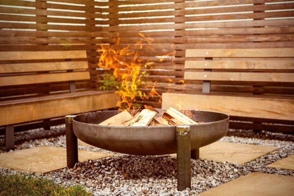 Feuerstelle mit Holz und Flammen in einem Garten mit Holzbänken und Steinboden