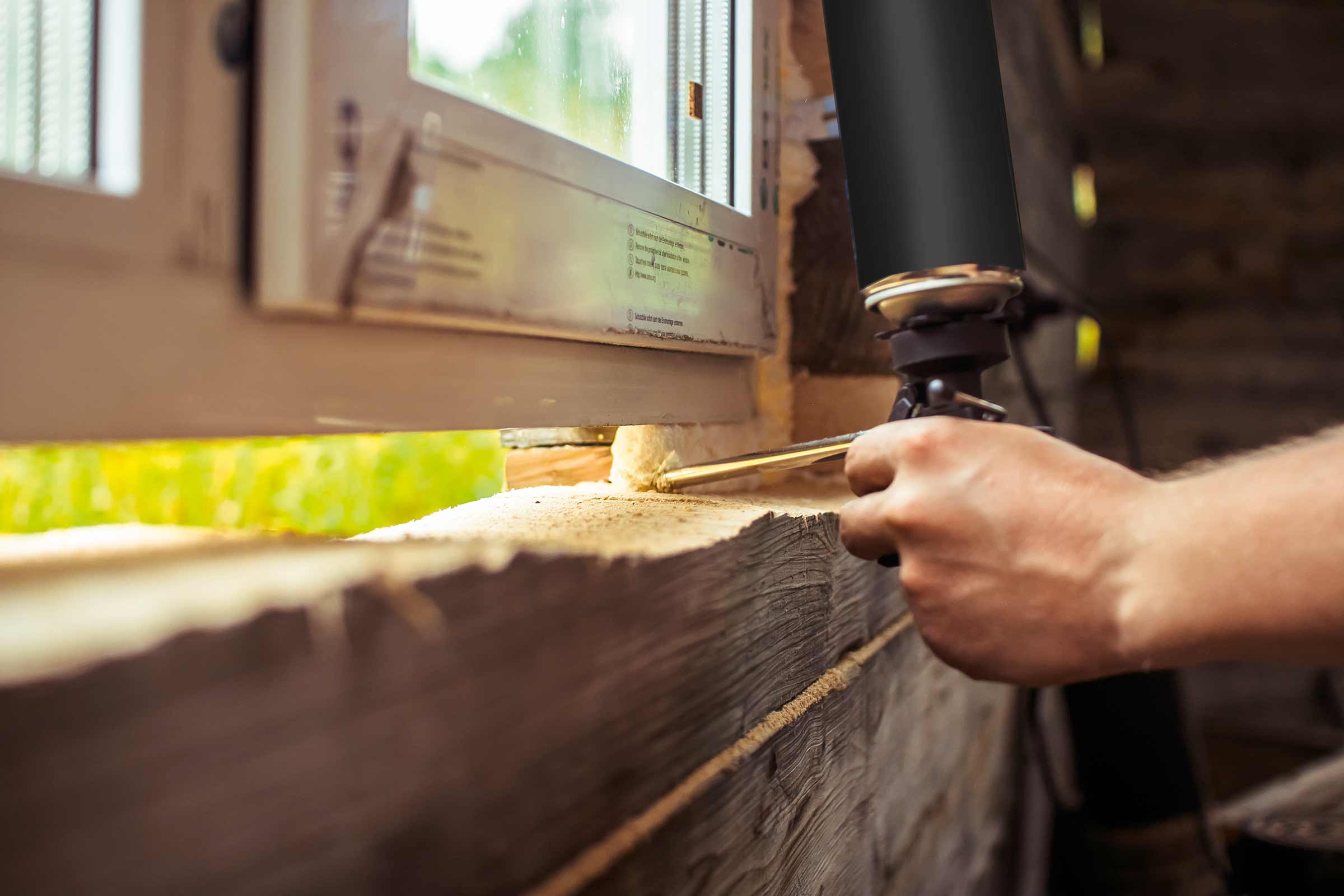 Eine Hand verwendet eine Schaumpistole, um ein Fenster zu isolieren.