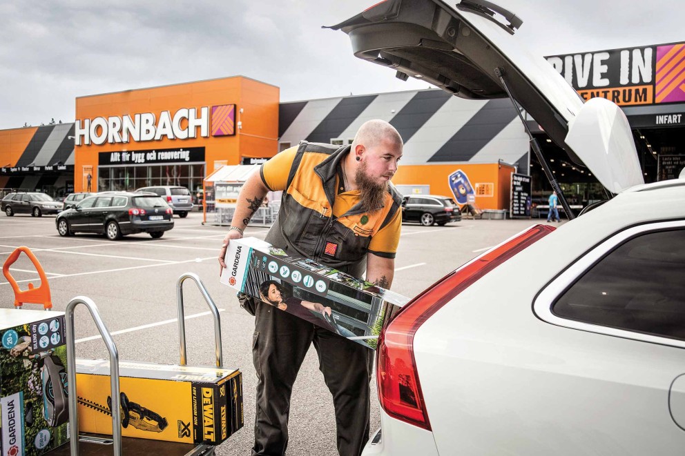 Ein Mann lädt Gartengeräte von Gardena und Dewalt in den Kofferraum eines Autos auf dem Parkplatz von Hornbach.
