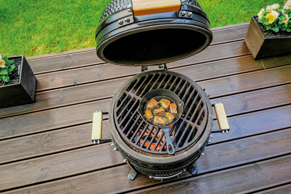 Keramikgrill mit offener Haube und Grillgut in einer Pfanne