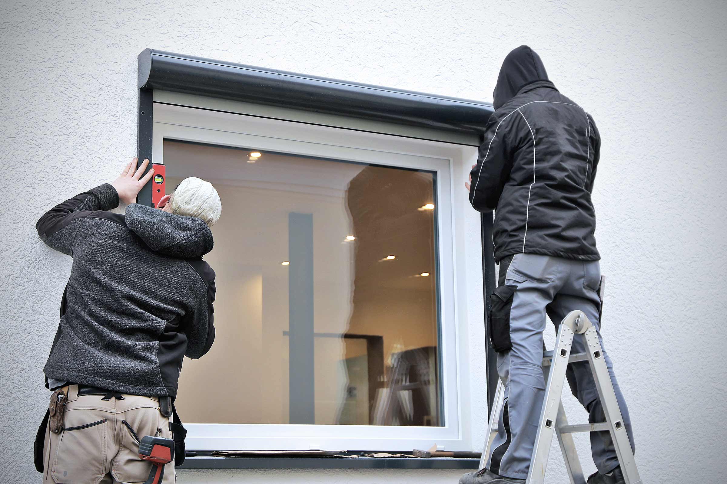 Zwei Monteure installieren einen Rollladen an einem Fenster.