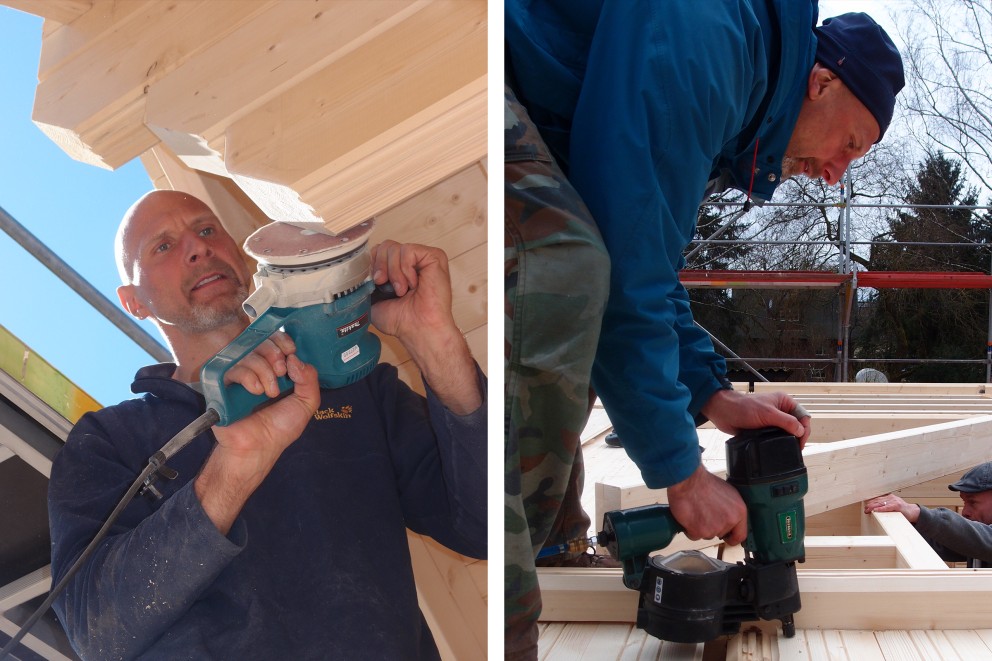Zwei Männer arbeiten an einer Holzkonstruktion, einer mit einem Schleifgerät, der andere mit einem Druckluftnagler.