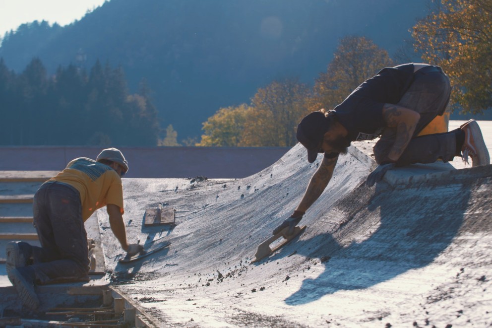 Bauarbeiter glätten das Beton des neuen Skateparks per Hand Bauarbeiter glätten das Beton des neuen Skateparks per Hand
