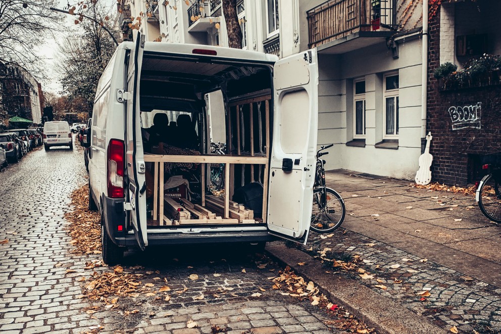 Van mit offenen Hecktüren. Straße mit Kopfsteinpflaster. Man sieht die Holzkonstruktion für Bett und Tisch. Van mit offenen Hecktüren. Straße mit Kopfsteinpflaster. Man sieht die Holzkonstruktion für Bett und Tisch.