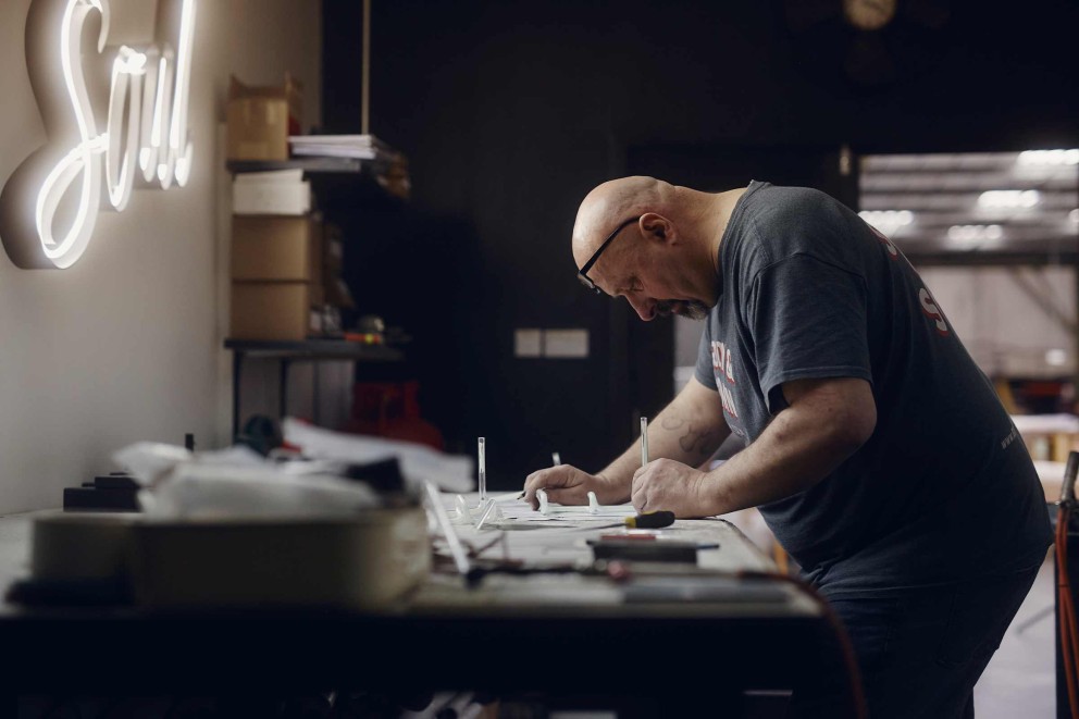 Paul Charlton, der in der Londoner Firma Goodwin & Goodwin Neon Logos und Schilder herstellt, skizziert auf Papier, wie er das Glasrohr biegen muss. Paul Charlton, der in der Londoner Firma Goodwin & Goodwin Neon Logos und Schilder herstellt, skizziert auf Papier, wie er das Glasrohr biegen muss.