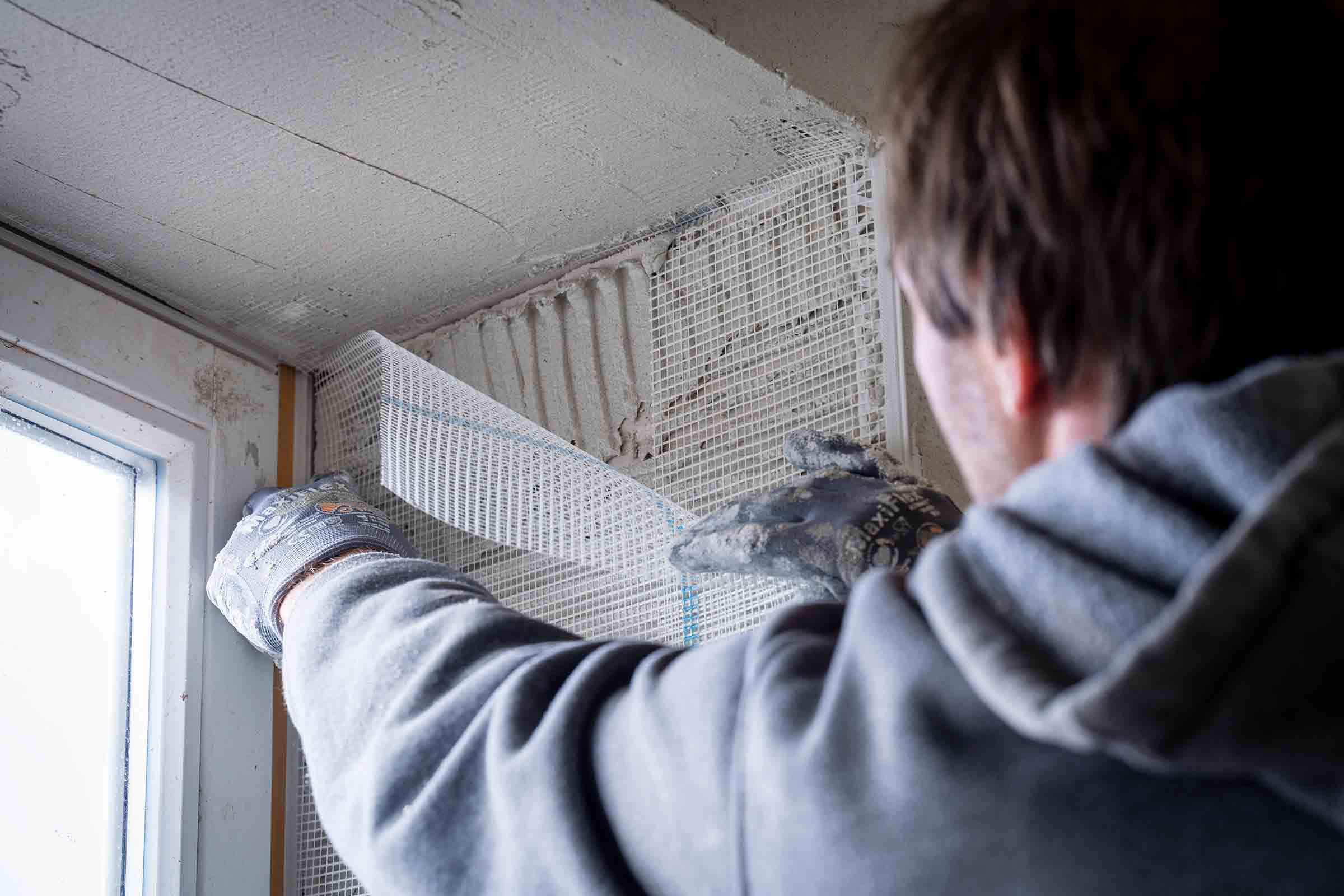 Mann befestigt Armierungsgewebe an einer Wand neben einem Fenster.
