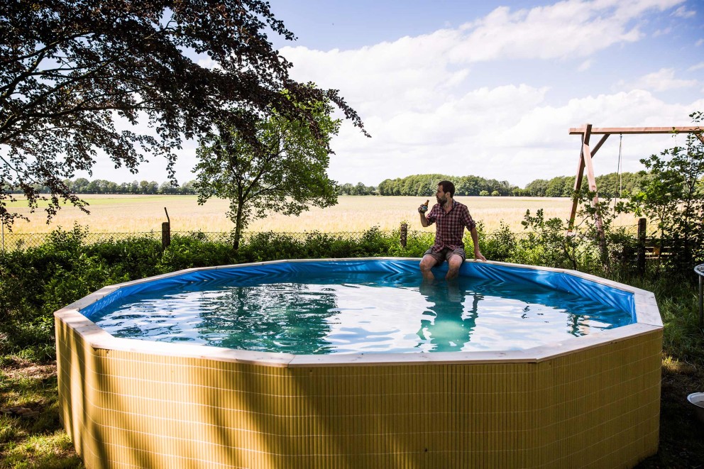 Autor Sascha Borrée sitzt am Rand seines selbst gebauten Palettenpools, mit den Füßen im kalten Wasser, und schaut in die Ferne. Autor Sascha Borrée sitzt am Rand seines selbst gebauten Palettenpools, mit den Füßen im kalten Wasser, und schaut in die Ferne.